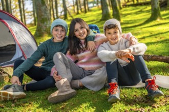 Bothers and sister sitting on the grass in the forest smiling at camera together enjoying camping