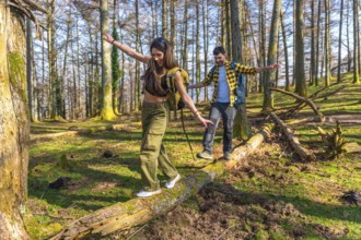 Hikers with backpacks carefully balancing on a fallen tree trunk while enjoying a hike through a