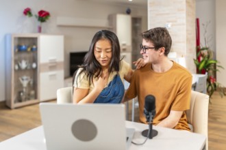 Asian woman and caucasian man recording a podcast at home, showcasing a modern lifestyle with