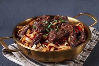Udon noodles with Mongolian beef, green onions and vegetables, in a brass pan, on a gray