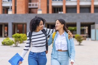 Frontal three quarter length photo of two multi-ethnic female student embracing walking along the