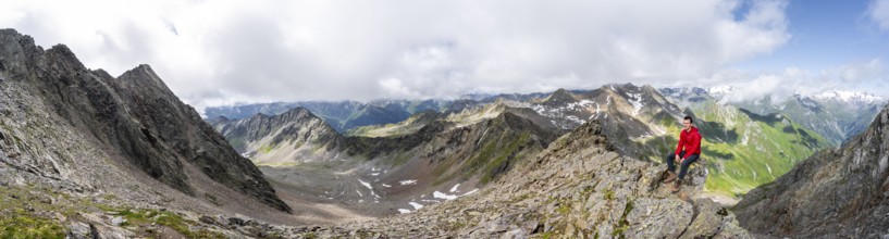 Panorama, mountaineer sitting on a rock, on a steep rocky ridge, on the summit of the Lasörling,