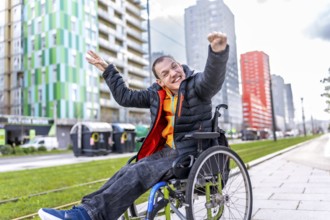 Portrait of a cheerful disabled man raising his arms in celebration, sitting in his wheelchair on a