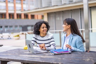 Two multi-ethnic female students using laptop sitting on the campus