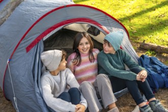 Sister and brothers enjoying sitting on camping tent in the forest
