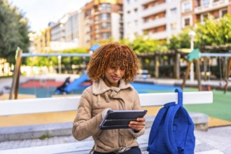 Latin young woman sitting on urban park bench using digital tablet