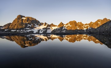 Rocky mountain peaks reflected in a small pond, mountain landscape with alpenglow at sunrise, at