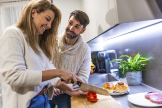 Young couple preparing dinner together, slicing tomatoes and making hamburgers in their modern