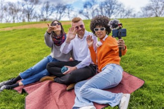 Three content creators waving and filming video with smartphone and external microphone in a park