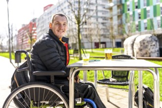 Young man in a wheelchair enjoys a refreshing drink with a friend at a table outside a cafe,