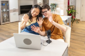 Multiethnic couple of content creators waving at their audience while recording a new episode of