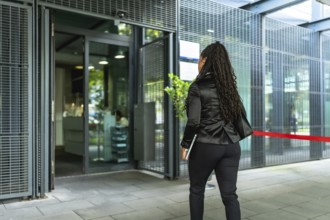 Rear view of an unrecognizable latin woman with long braids entering to a modern business building