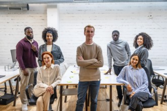 Portrait of a confident man standing next to coworking colleagues sitting around a table