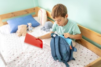 Schoolboy prepares his backpack for school sitting on bedroom and preparing for school
