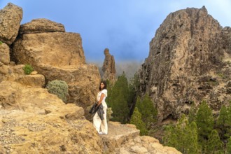 Woman standing on a rocky viewpoint enjoying the scenic landscape of roque nublo, a volcanic rock