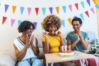 Excited african american young woman celebrating birthday with friends at home