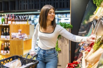 Young woman shopping for groceries, choosing fresh organic vegetables from a display shelf in a
