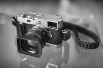 Leica M11 with Kamerakraft Grip and RocknRoll carrying strap standing on glass table, black and
