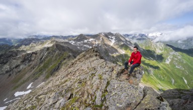 Mountaineer sitting on a rock, on a steep rocky ridge, on the summit of the Lasörling, view of the