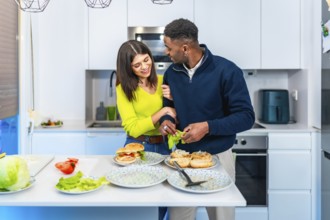 Young multiethnic couple enjoying quality time together while preparing delicious burgers in their