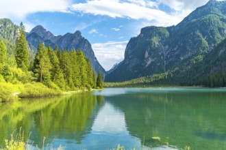 Stunning alpine landscape reflecting on lake dobbiaco's emerald waters, surrounded by lush