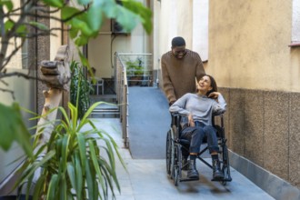 African man pushing wheelchair of disabled colleague outside a coworking space with plants