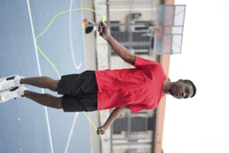 Vertical photo of an energetic african teenager jumping rope in an urban basketball court