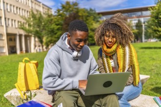 African student and latin female colleague using laptop sitting outside the campus