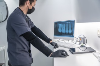 Dentist wearing mask and gloves analyzing a teeth x ray on a computer in a modern dental clinic
