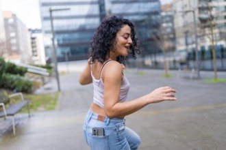 Carefree young woman dancing in the city with smartphone in her pocket, enjoying music and urban