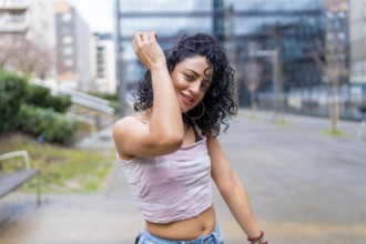 Carefree young woman enjoying music through headphones, dancing in a city park, expressing joy and