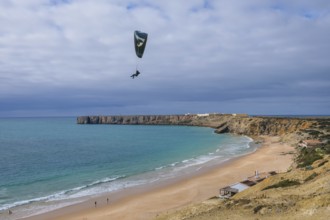 Sagres, Algarve, Portugal - Paraglider flying on the town beach Praia da Mareta, behind the sea
