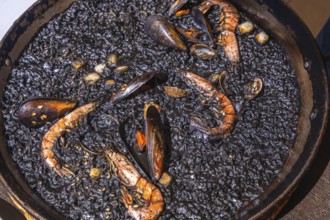 Close up of black paella with shrimps, mussels and other seafood, cooked and ready to be served in