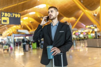 Businessman waiting for his flight, talking on the phone and holding a coffee while pulling his