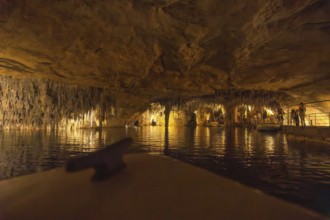 Tourists enjoying a boat trip on the martel lake inside the drach caves, illuminated by colorful
