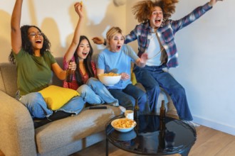 Group of young multi ethnic people enjoying a sports event on television, drinking beer and eating