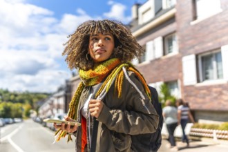 Distracted young latin woman with warm clothes using phone in the city
