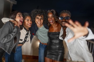 Multi-ethnic friends embracing and partying in a private rooftop at night