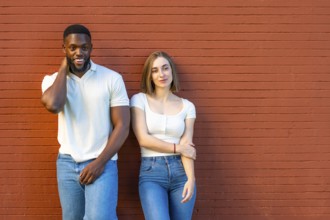 Horizontal photo with copy space of a shy multi-ethnic couple in denim clothes leaning on urban