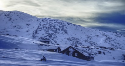 Snow-covered landscape with individual houses against a mountain backdrop in the morning light