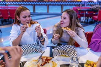 Two friends enjoying pizza at a bowling alley restaurant, celebrating a fun weekend together