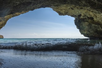 Gentle waves lapping at the shore, viewed from beneath a rocky overhang on a sunny beach in cala