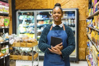 Confident saleswoman holding a notebook and smiling in an organic supermarket aisle, surrounded by