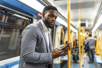 Young businessman using smartphone while commuting on subway train, holding handrail and looking