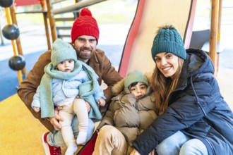 Smiling parents and children wearing winter clothes enjoying a winter day on a playground slide