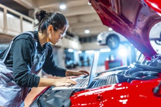 Young female mechanic using a laptop while inspecting a car engine in a professional auto repair