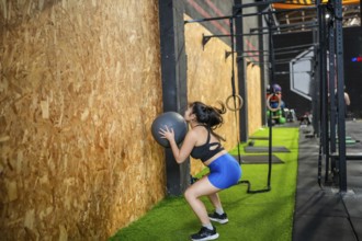 Chinese fit woman training with medicine ball in the gym squatting and throwing up the ball