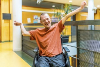 Successful man with disability celebrating in a modern coworking sitting on wheelchair and raising