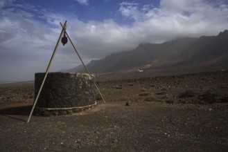 Stone fountain in lonely, barren volcanic landscape near Cofete in front of cloudy mountains,