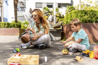 Playful mother and sons having fun sitting on the ground and playing with toys in a park